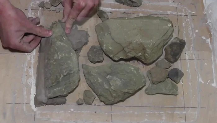 Arrange rocks in a natural formation on the plywood, filling gaps with clay to extend rocks and create crevices. Use a tool to carve the clay for a natural look.